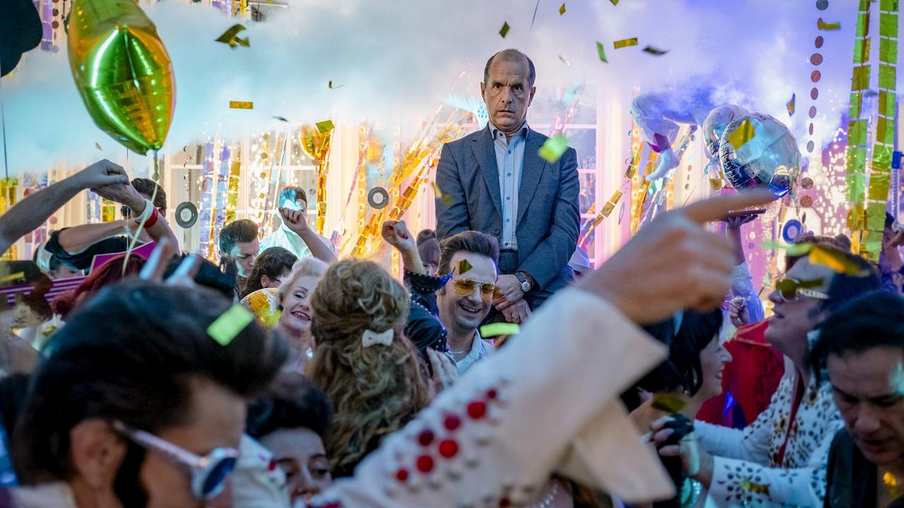 Christoph Maria Herbst als Event-Manager Dieter Salzmann, mit entgeisteter Miene blickt er über das ausgelassen feiernde Partygäste