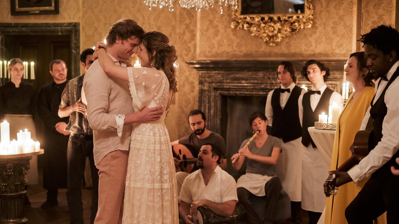 Lasse und Leonie beim romantischem Tanz in einem der Schlossräume, Kellner und Kellnerinnen, Musizierende schauen den beiden freundlich lächelnd zu