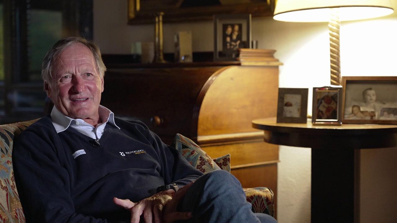 © ORF/ORF Sport Franz Klammer sitzt in einem gemütlich beleuchteten Wohnzimmer zwischen Erinnerungsfotos und spricht in einem Interview.