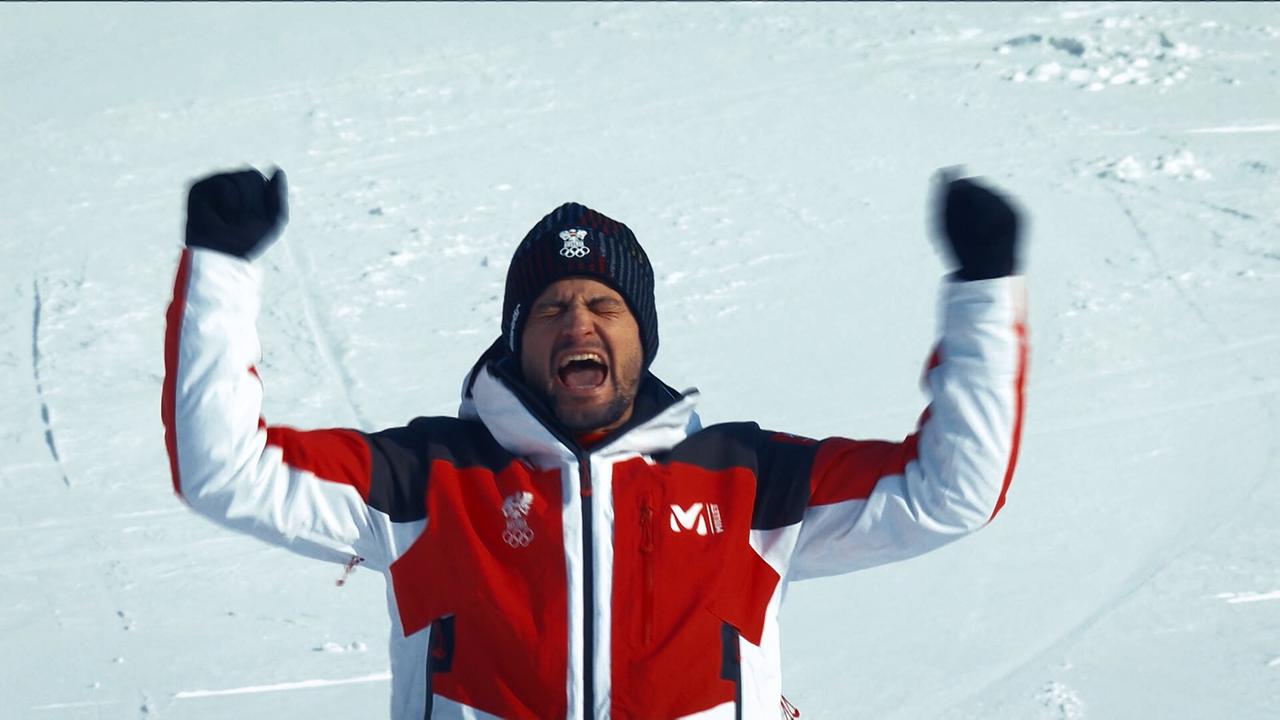 © ORF/ORF Sport Johannes Strolz hebt auf einer schneebedeckten Fläche triumphierend beide Arme.