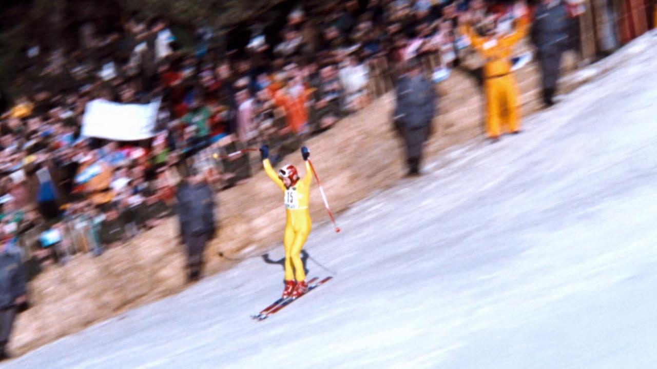 © ORF/ORF Sport Franz Klammer im gelben Skianzug fährt jubelnd auf einer Rennstrecke an dicht gedrängten Zuschauern vorbei.