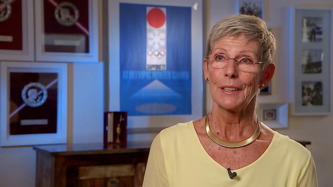 © ORF/ORF Sport Trixi Schuba wird in einem Raum mit zahlreichen olympischen Erinnerungsstücken und Auszeichnungen interviewt.