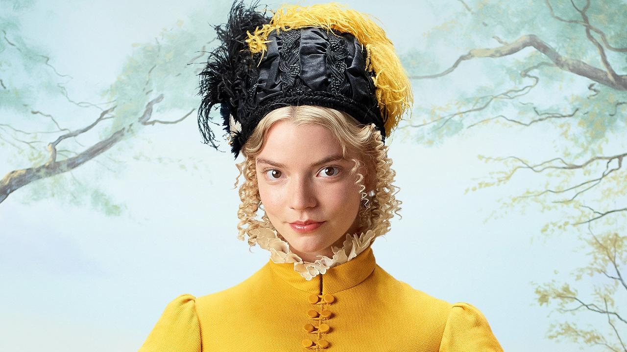 Anna-Taylor-Joy als Emma Woodhouse, blond gelockt mit gelbem hochgeschlossenen Kleid und einem schwarzen Hut mit gelben und schwarzen Federn