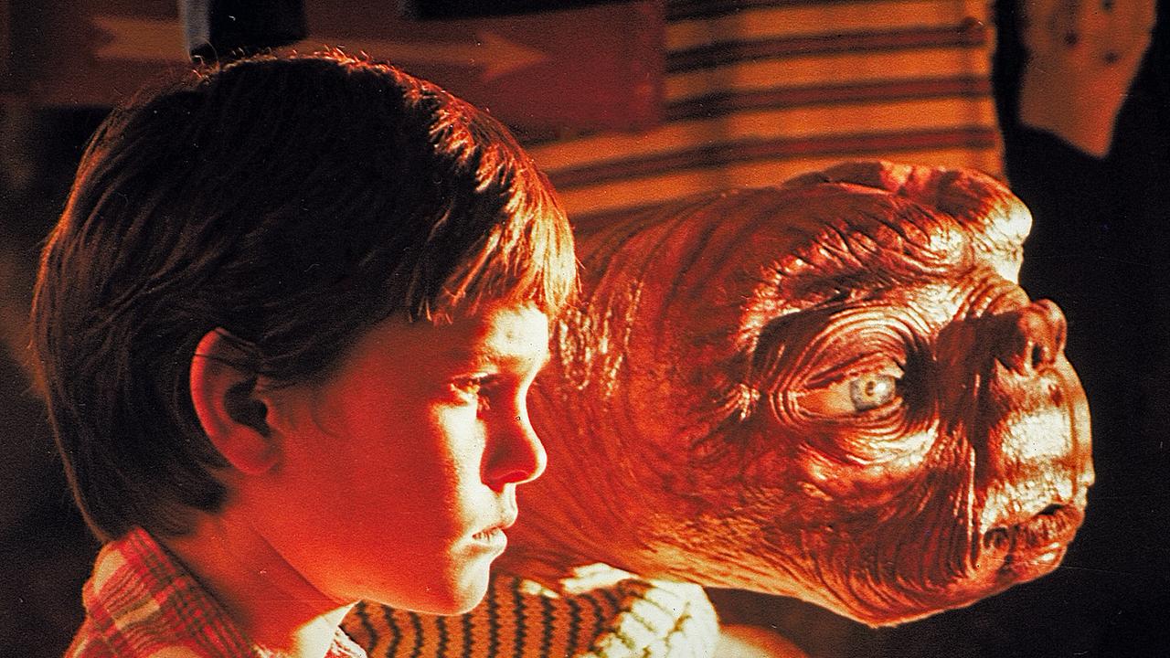 Henry Thomas als Elliot und der Außerirdische E.T. stehen in einenm Zimmer und schauen in der Nacht durch die Jalousie, durch die ein grelles Licht von draußen fällt
