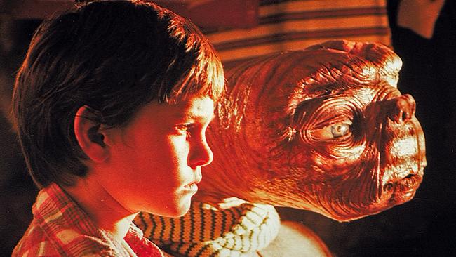 Henry Thomas als Elliot und der Außerirdische E.T. stehen in einenm Zimmer und schauen in der Nacht durch die Jalousie, durch die ein grelles Licht von draußen fällt