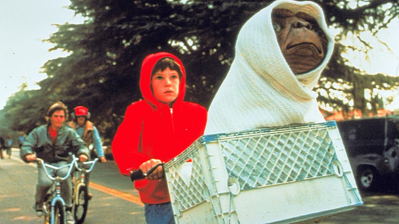 Henry Thomas fährt als Elliot auf seinem Rad, im Korb vor ihm sitzt der Außerirdische E.T. vermummt, das Rad hebt sich in die Lüfte, hinter ihnen folgen ihnen zwei Burschen auf Rädern