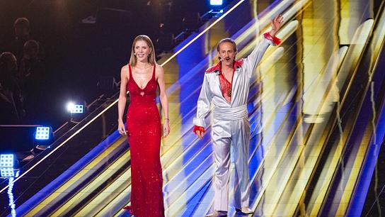 Victoria Swarovski in roter Abendrobe und Michael Ostrowski in weißem Satinanzug und rotem Spitzenhemd auf der ESC-Bühne