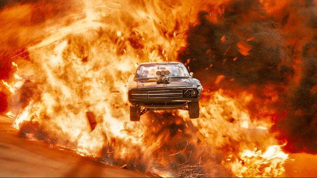 Ein schwarzer Sportwagen fliegt durch die Luft auf die Kamera zu, im HIntergrund die Feuerwolke einer großen Explosion