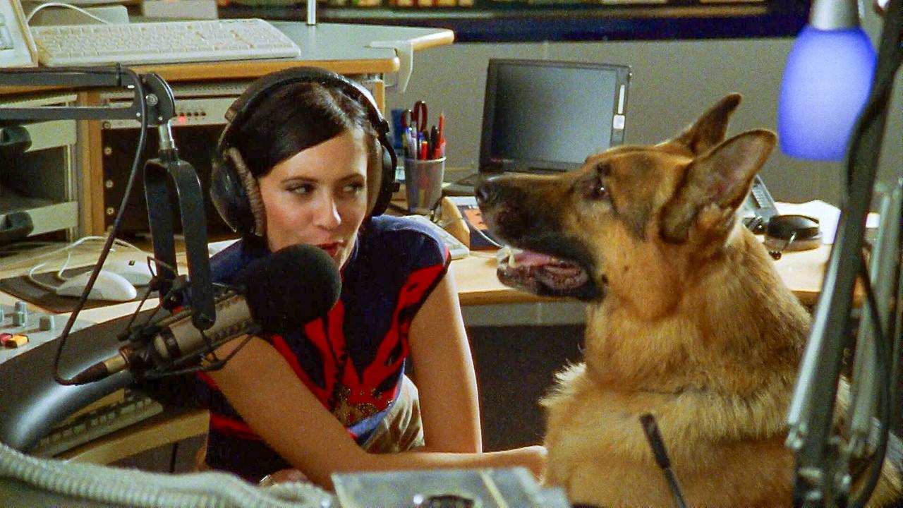 Rex sitzt neben Doris Golpashin, die vor einem Mikro sitzt und Kopfhörer trägt, in einem Radiostudio.