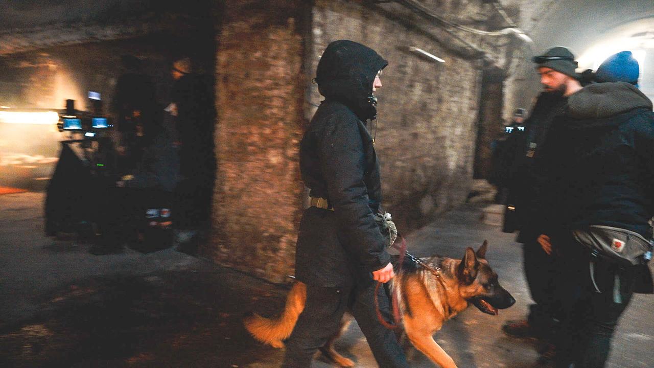 Ein Hundeführer geht in der Drehpause mit dem Schäferhund Rex durch einen dunklen Gang, begleitet von einem Kamerateam.