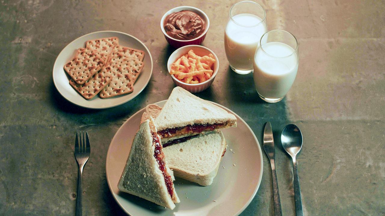 Ein gedeckter Platz am Tisch - Marmelade-Sandwiches und Knäckebrot auf Tellern, eine Mousse au chocolat und Salzgebäck in Schalen, dazu zwei Gläser Milch