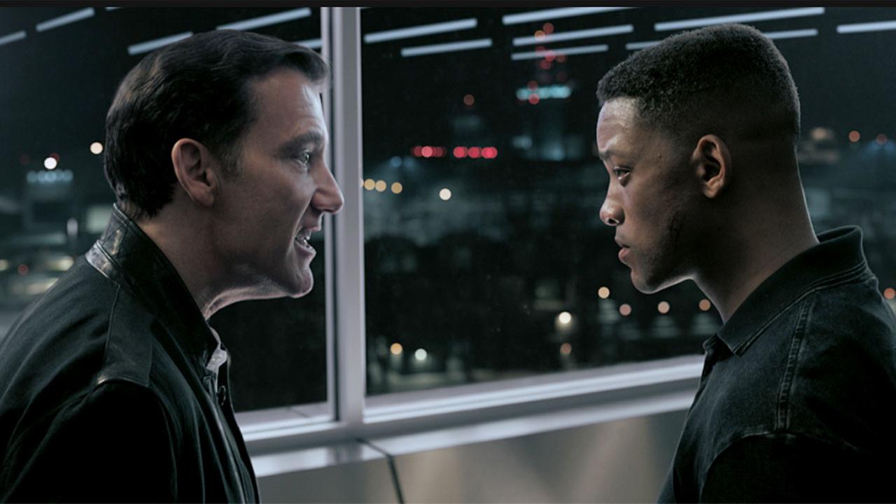 © ORF/Pro7/© 2019 Paramount Pictures Clive Owen als Clay Verris und Will Smith als Henry Brogan vor der Scheibe eines Kontrollraums mit blinkenden Lichtern unterhalten sich die beiden ernst miteinander, beide tragen dunkle futuristische Uniformen