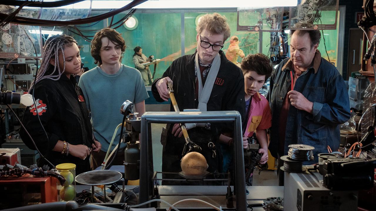 © ORF/Sony Pictures/CTMG/Jaap Buitendijk Drei Jugendliche und ein Mann beobachten einen Mann mit Brille, der in seiner Werkstätte einen Apparat testet