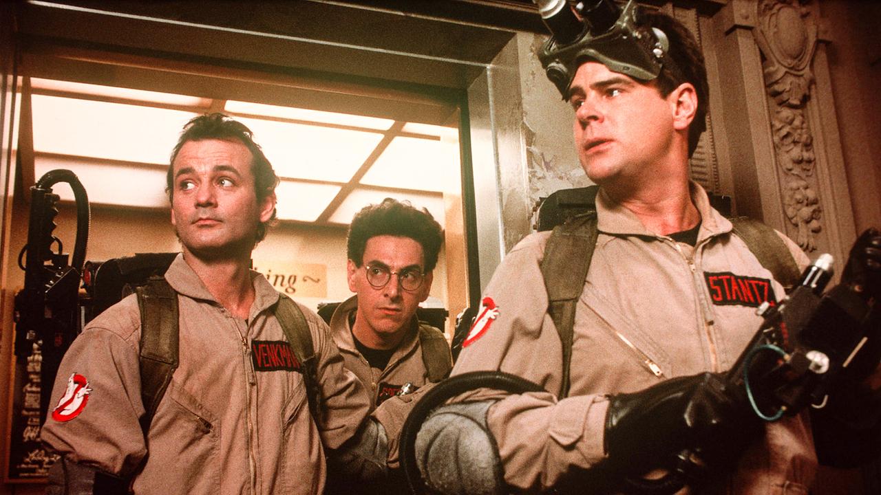 Bill Murray, Harold Ramis und Dan Aykroyd kommen auf Geisterjagd in ihren beigefarbenen Overalls mit technischer Ausrüstung aus einem Lift 