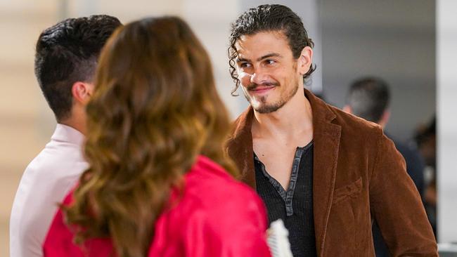 Gael Martinez mit schwarzem Shirt und brauner Jacke, unterhält sich im Stehen mit einer Frau mit pinkfarbener Jacke und einem Mann im weißen Hand und lächelt freundlich