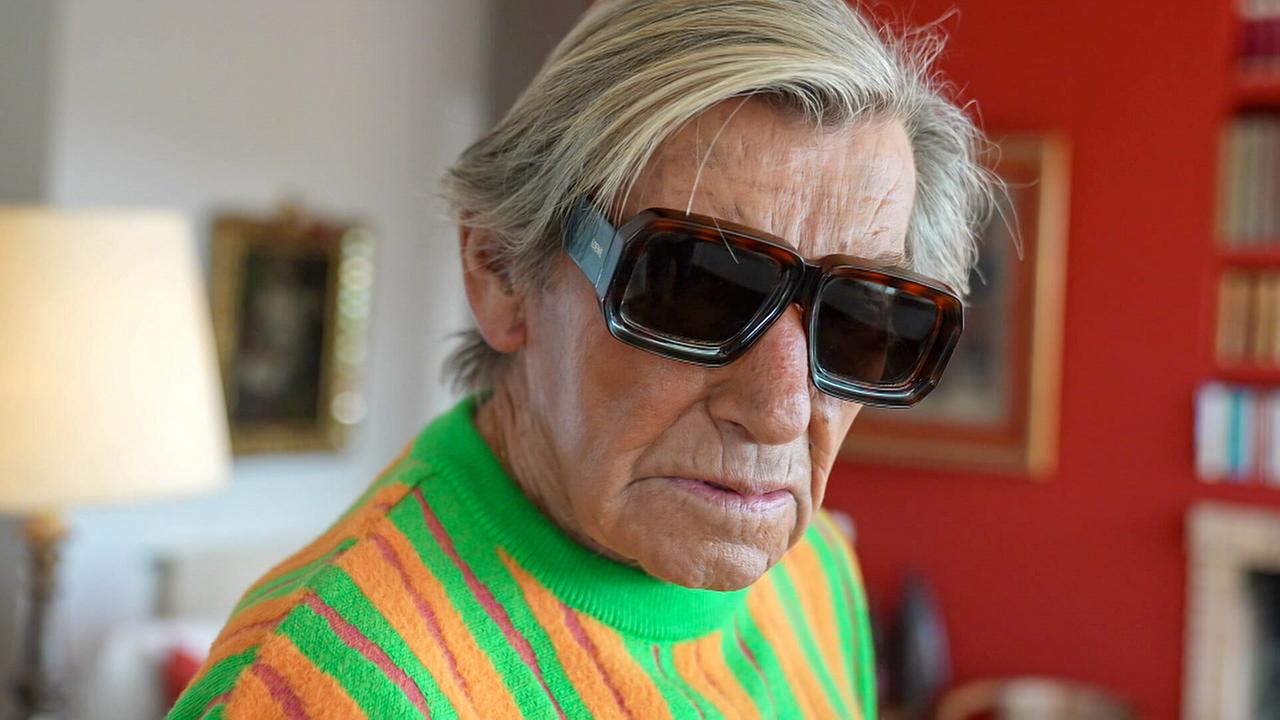 Influencer mit 92: 'The Spanish King' Andrés Garcia-Carro, mit cooler Sonnenbrille und grellbuntem Pulli steht er in seinem stilvol modern eingerichteten Wohnzimmer 