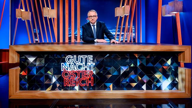 Peter Klien sitzt an einem Studiotisch mit der Aufschrift „Gute Nacht Österreich“ vor einer modernen, blau beleuchteten Kulisse.
