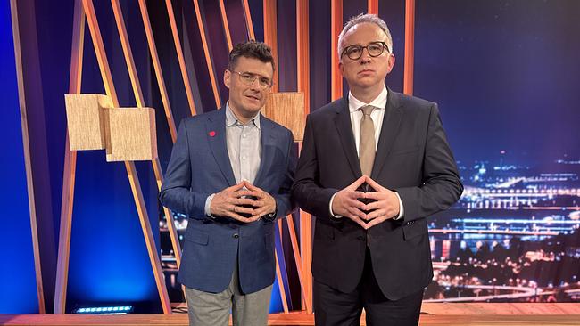 © ORF/Gebhardt Productions Manuel Rubey und Peter Klien stehen nebeneinander im "Gute Nacht Österreich"-Studio und halten ihre Hände die Fingerspitzen berührend vor ihrem Körper.