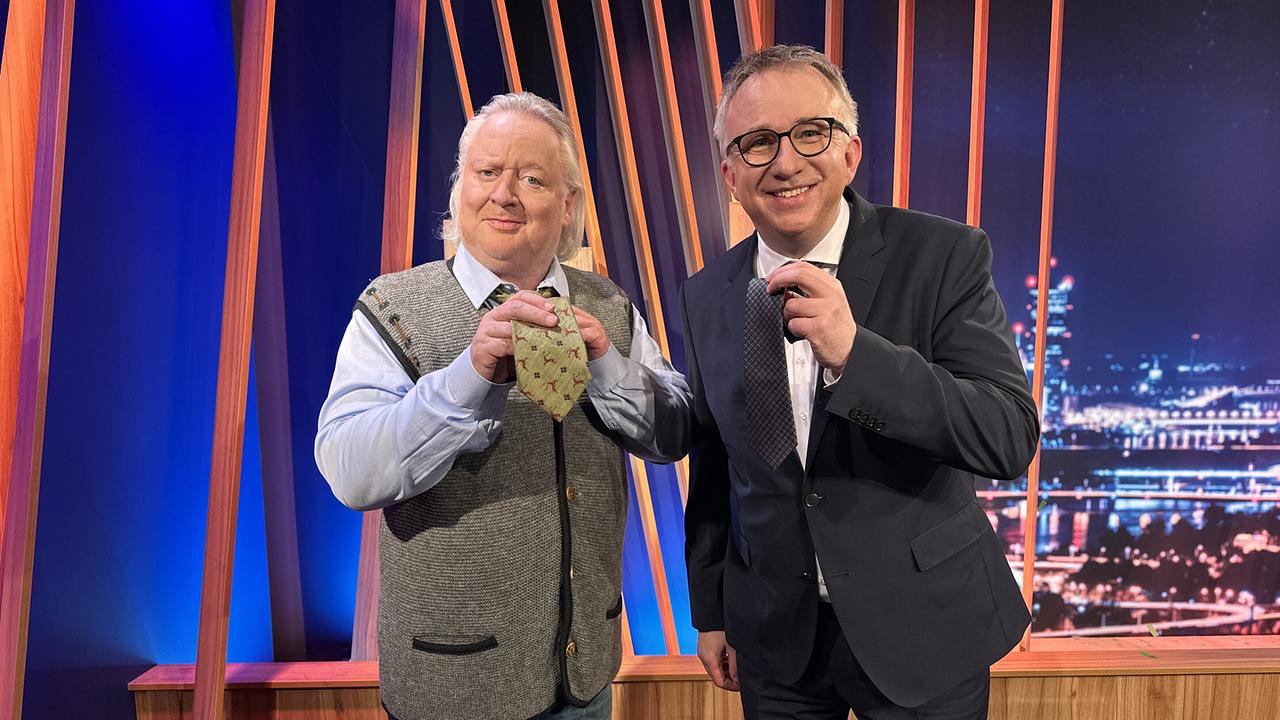 © ORF/Gebhardt Productions Gregor Seberg und Peter Klien stehen im "Gute Nacht Österreich"-Studio und halten jeweils eine Krawatte in die Kamera.