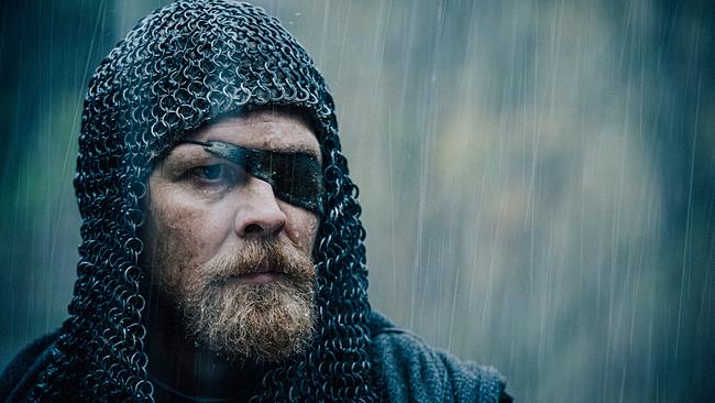 Großaufnahme von Gijs Naber als bärtiger Hagen von Tronje mit mittelaltericher Kettenhaube und Augenklappe, im Regen blickt er ernst 