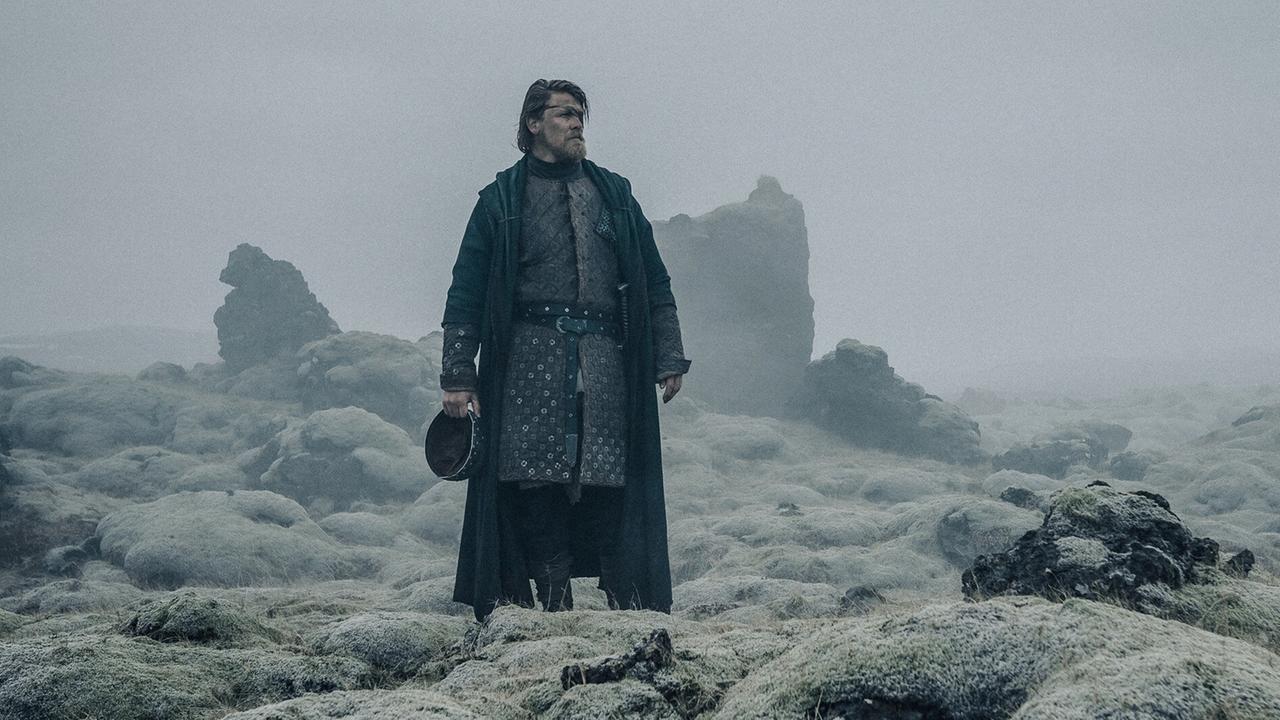 © ORF/Constantin Film Gijs Naber als Hagen von Tronje steht in mittelalterlicher Rüstung in einer nebelverschleierten, steinigen Landschaft, die Felsen sind karg mit Flechten bedeckt