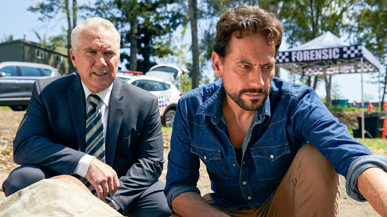 © ORF/Disney/ABC/Julian Panetta Bryan Nichols in einem grauen Anzug mit Hemd und Krawatte und Harrow im Jeans-Hemd, beide knien am Flussufer und untersuchen die tote Frau