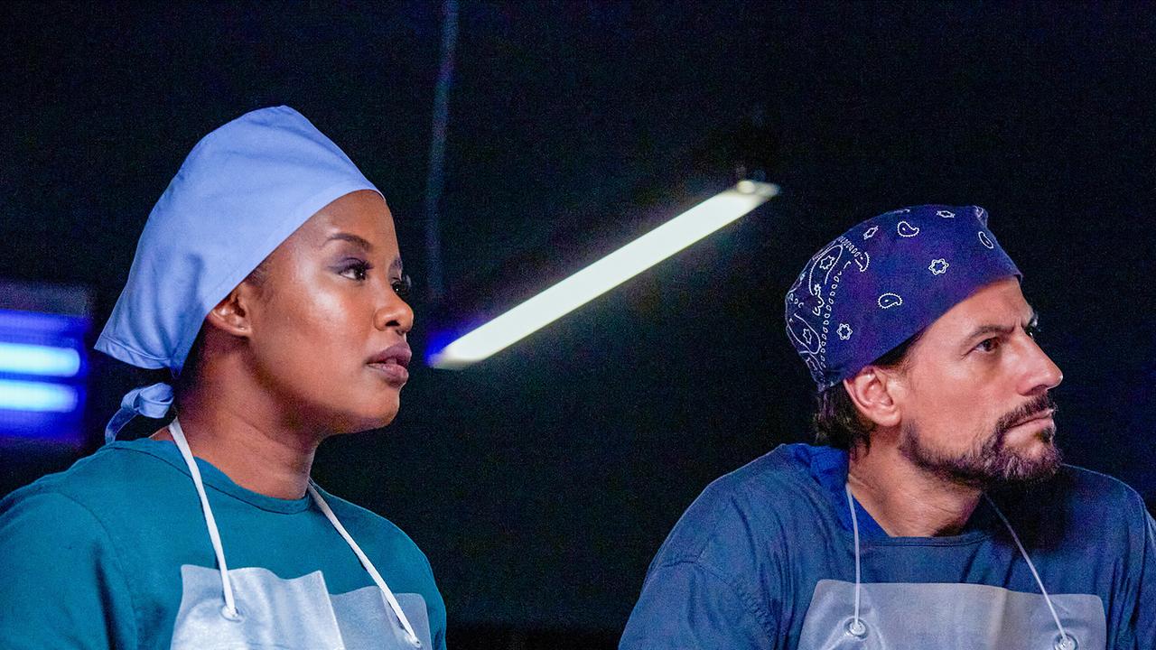 © ORF/Disney/ABC/Julian Panetta Edwina Gharam und Harrow in Operations-Bekleidung bei der Obduktion, beide hören anscheinend jemandem interessiert zu, der ihnen gegenübersteht
