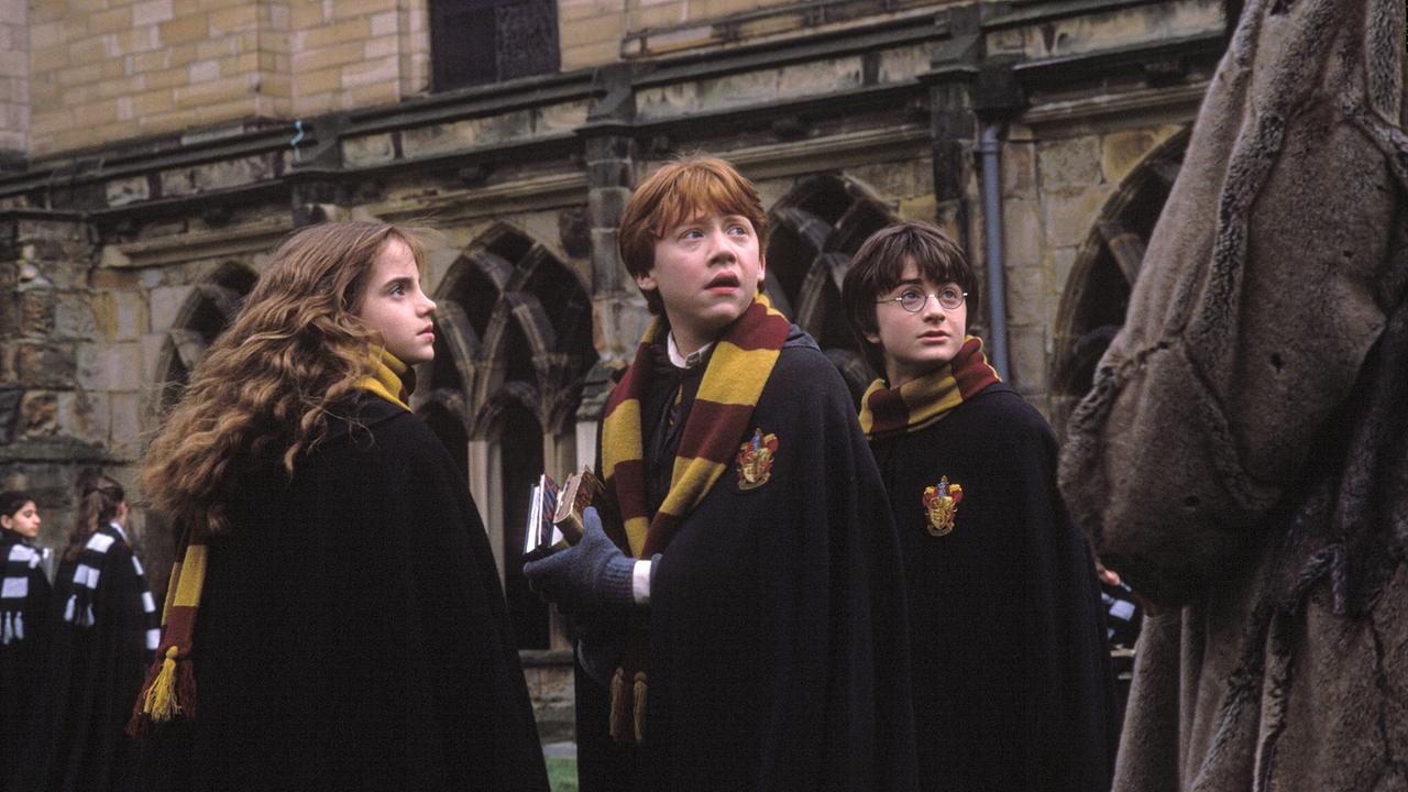 Hermine Granger, Ron Weasley und Harry Potter in Schuluniformen mit rot-gelb-gestreiften Schals im Hof von Hogwarts