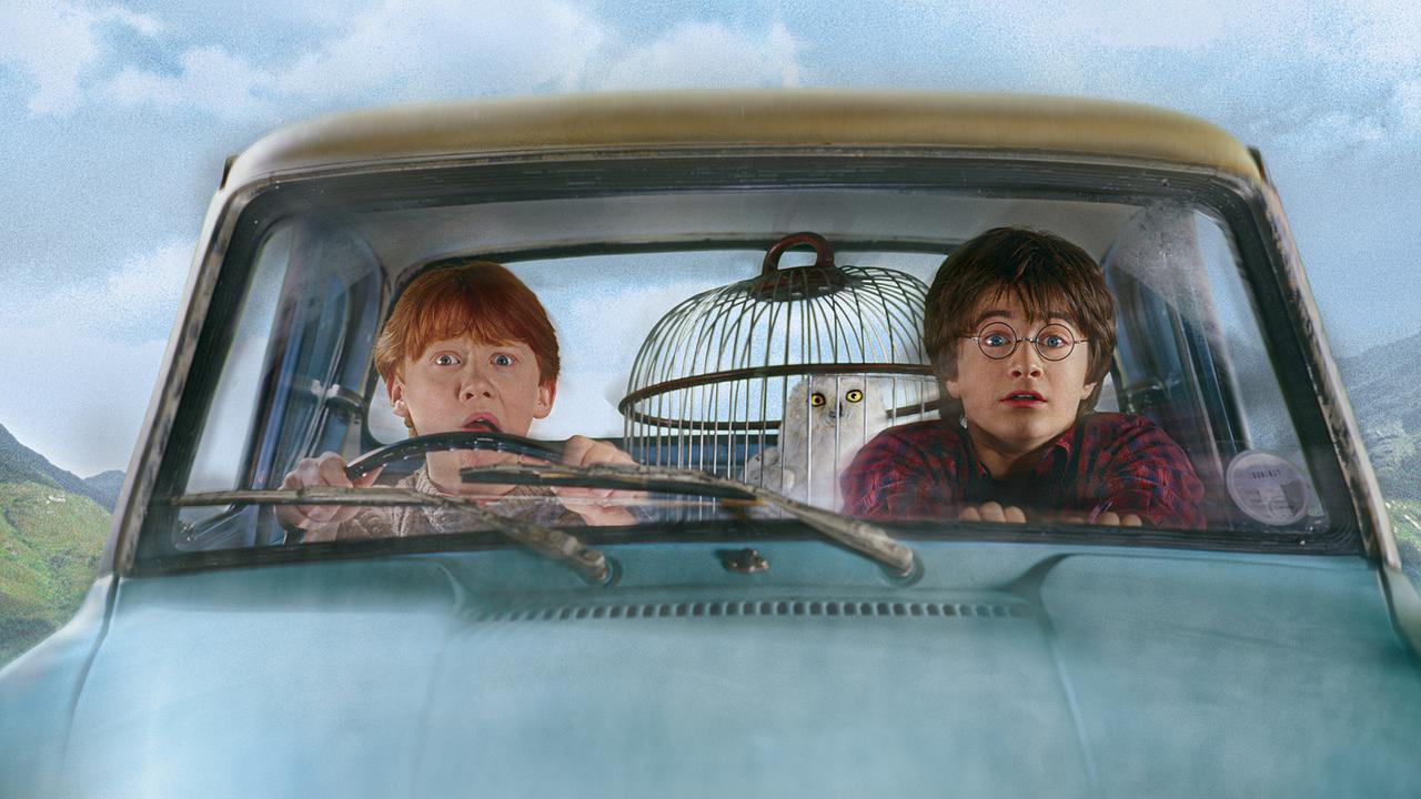 Ron Weasley am Steuer eines hellblauen, fliegenden Autos, Harry Potter sitzt am Beifahrersitz daneben, hinten auf der Rückbank ein Vogelkäfig mit einer weißen Eule