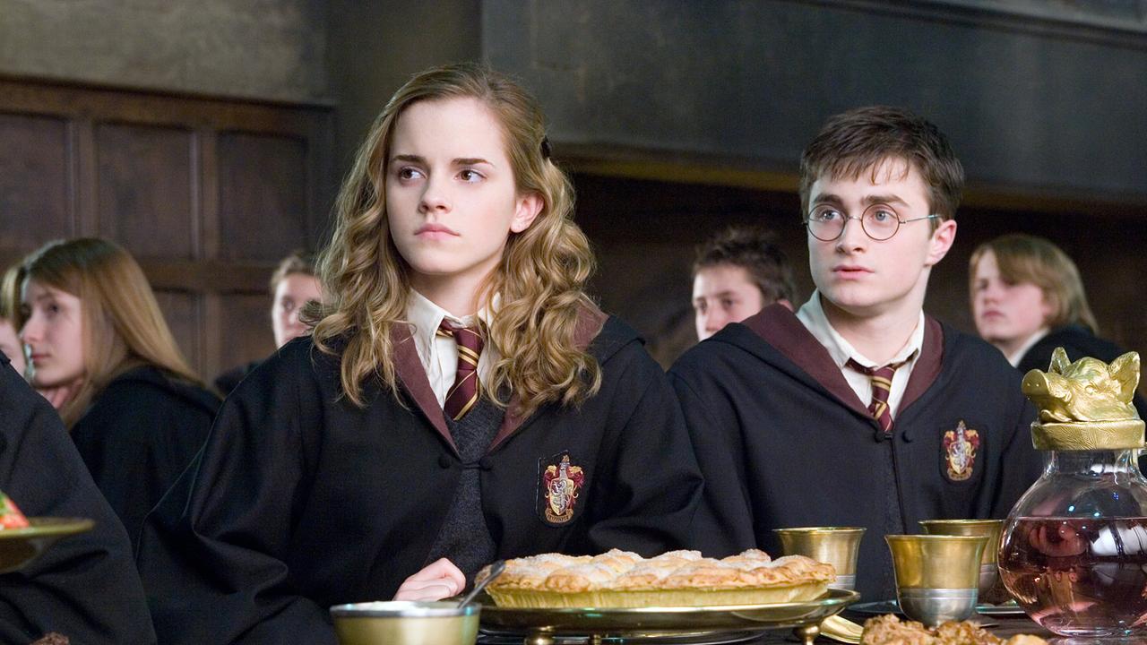 Hermine Granger und Harry Potter sitzten nebeneinander beim Essen im Speisesaal der Zauberschule, alle Schülerinnen und Schüler schauen in dieselbe Richtung und folgen einer Ansprache