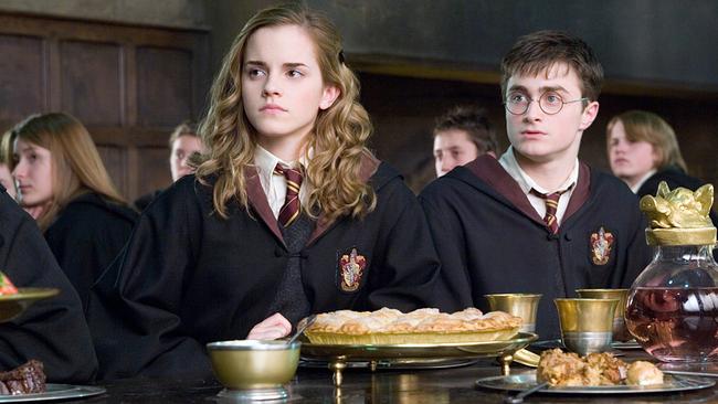 Hermine Granger und Harry Potter sitzten nebeneinander beim Essen im Speisesaal der Zauberschule, alle Schülerinnen und Schüler schauen in dieselbe Richtung und folgen einer Ansprache
