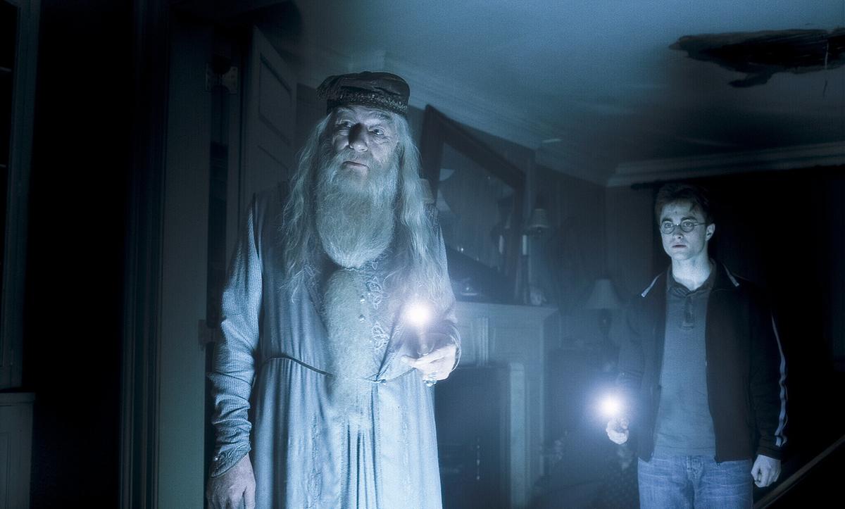 © ORF/Warner Bros. Pictures Albus Dumbledore mit langem weißen Bart und weißen Haaren geht mit Harry Potter durch einen dunklen Raum, beide tragen eine Kerze in der Hand und blicken in dieselbe Richtung vor sich hin