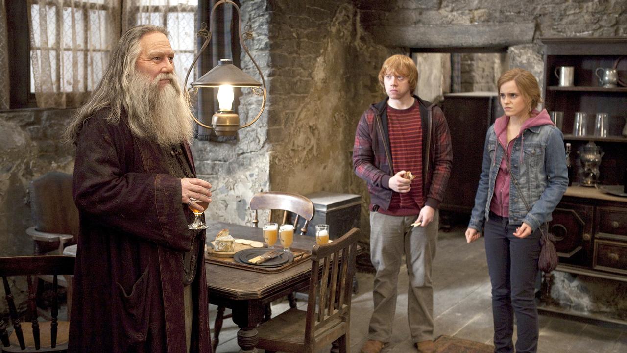 © ORF/TELE-München Ron Weasley und Hermine Granger besuchen Aberforth Dumbledore, er steht in seinem historisch eingerichteten, alten Wohnzimmer mit einem Glas am Tisch, Ron und Hermine folgen interessiert seinen Worten