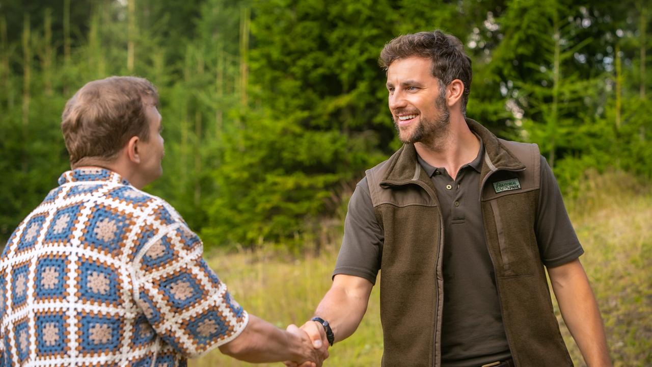 Marc und Ben begrüßen einander mit einem Handschlag auf einer Lichtung am Waldrand.