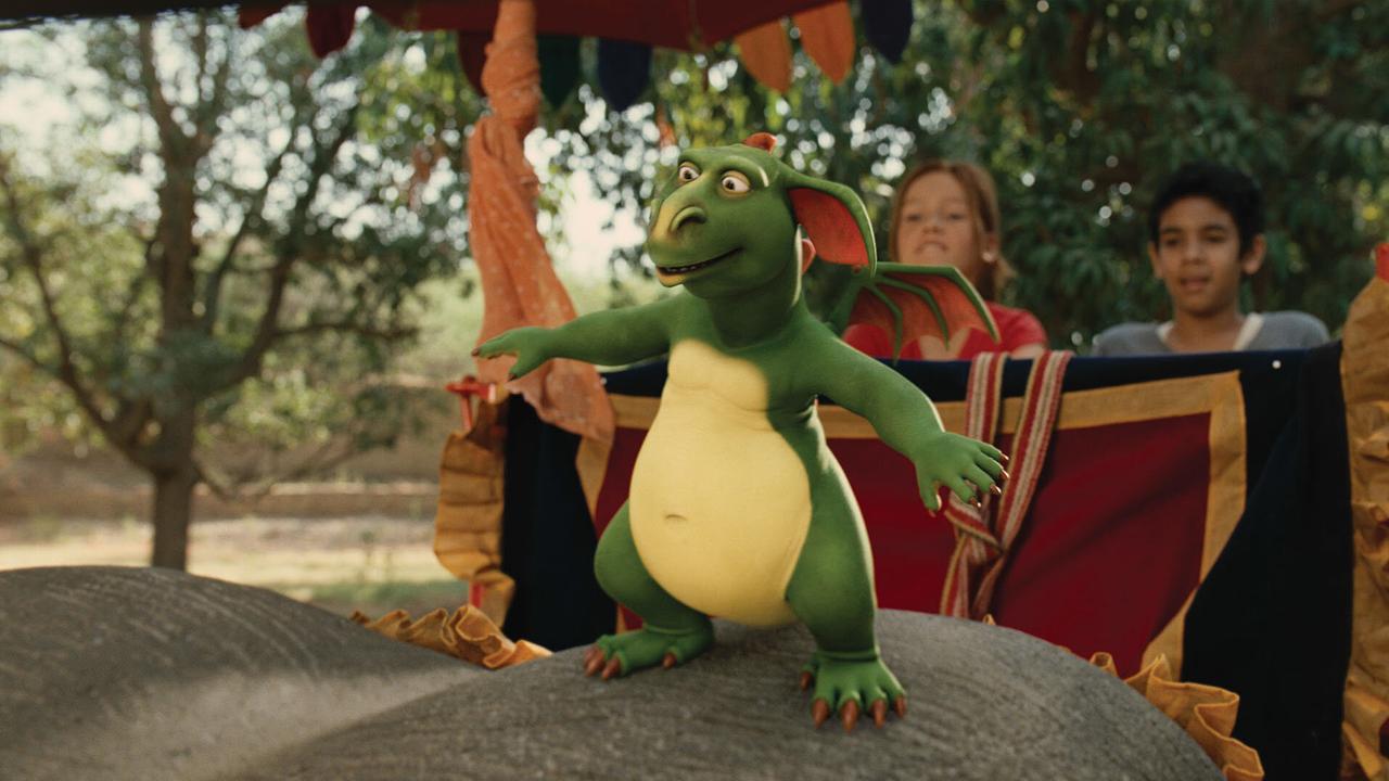 Ein grüner Flugdrache mit gelbem Bauch balanciert auf dem Rücken eines Elefanten, hinter ihm sitzt ein Mädchen und ein Bub in einer Kabine und schauen ihm zu