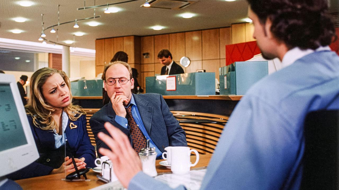 © ORF/DOR Film/Petro Domenigg In einer Bankfiliale sitzen Margit Kracal und Herbert Kracal dem Bankangestellen Eberl gegenüber und hören ihm aufmerksam zu.