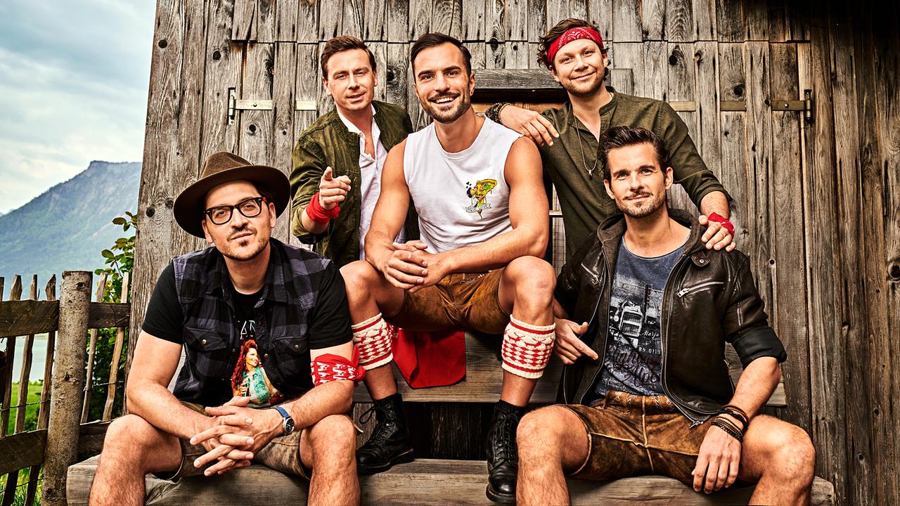 © ORF/Constanze Grießler/Mountain Crew Die Mitglieder von Mountain Crew sitzen auf einer Bank vor einer Scheune, in Lederhosen, Shirts und Jacken posieren sie für ein Gruppenfoto