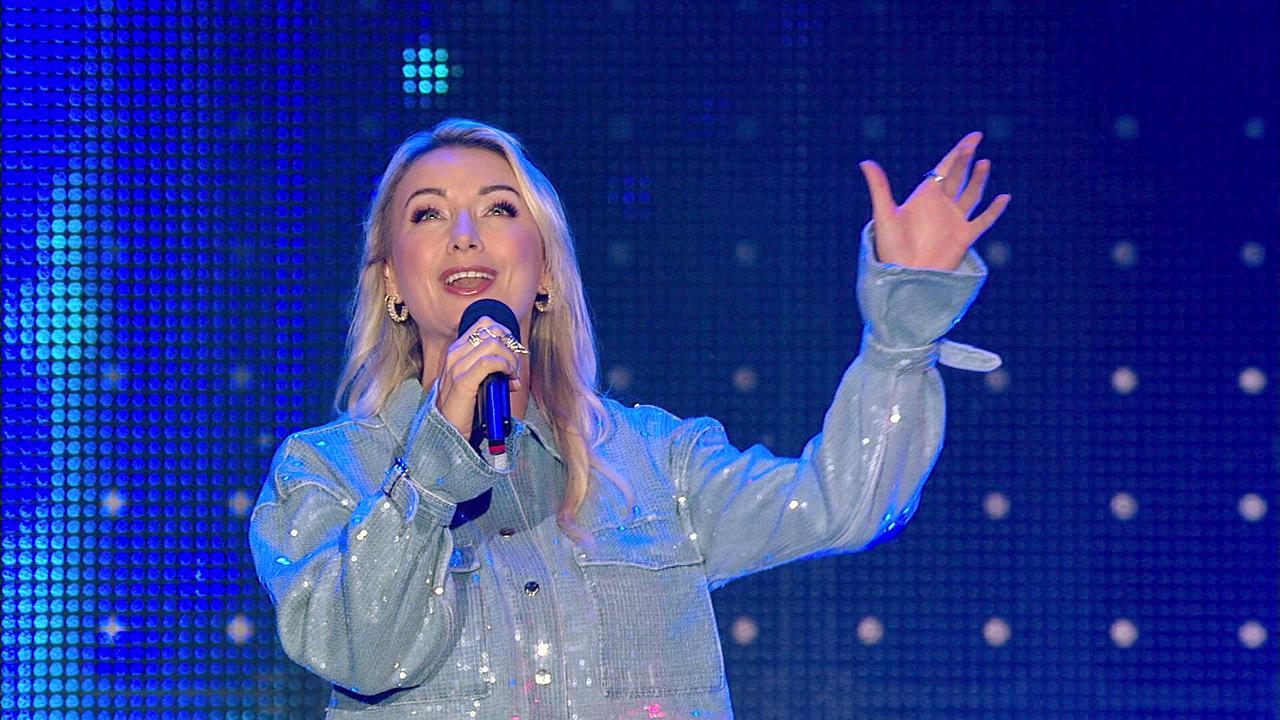 © ORF/Constanze Grießler Anna-Carina Woitschak in glitzernder Jeans-Jacke mit Mikrofon in der Hand singt sie auf der blau beleuchteten Bühne der 'Starnacht'