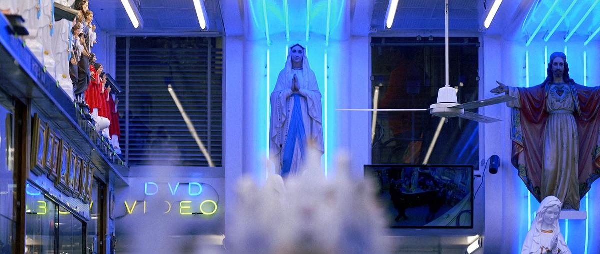 Ein Souvenirladen in Lourdes, darin sind mit Neonröhren blau beleuchete Statuen von Maria und Jesus ausgestellt