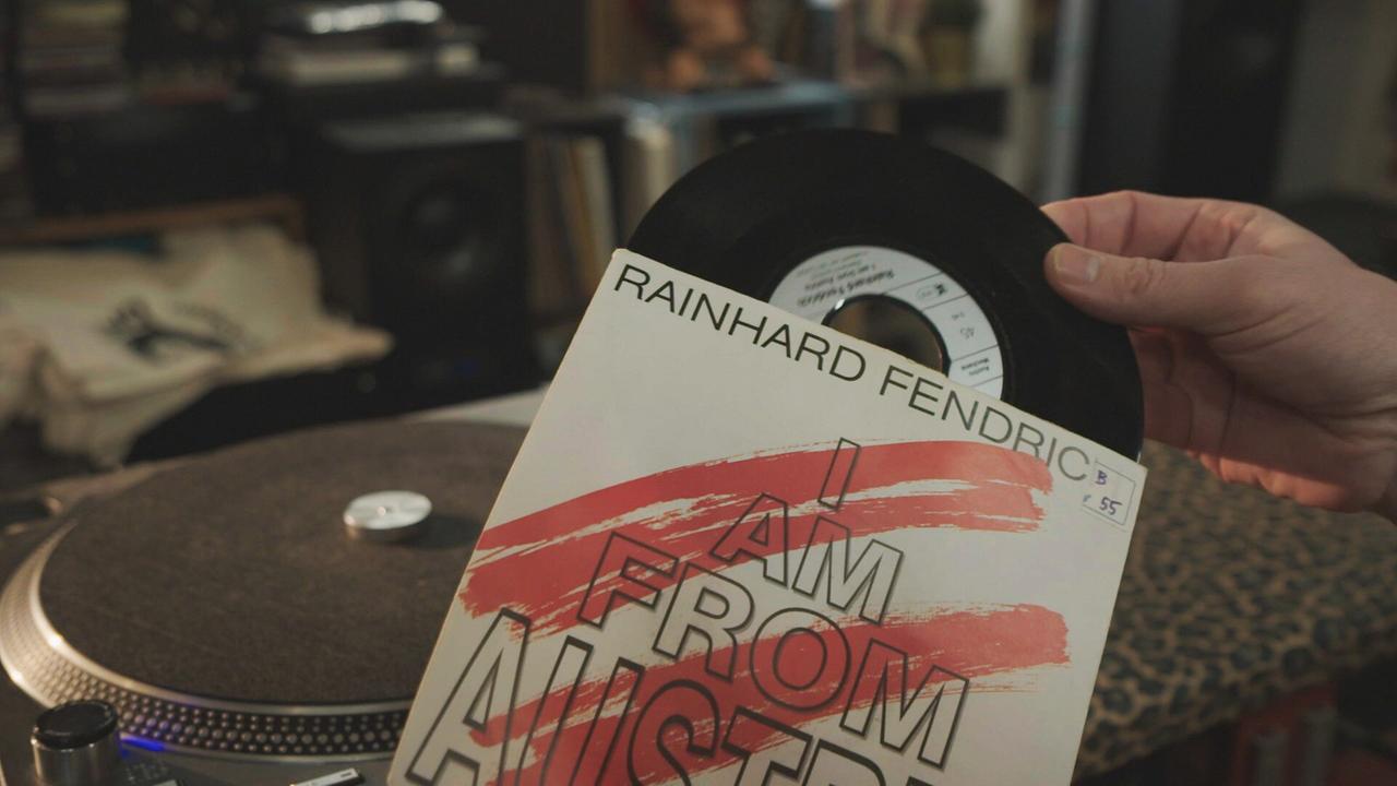 © ORF/LV Eine Hand zieht die Single "I am from Austria" aus dem Schallplattencover, dahinter steht ein Plattenspieler.