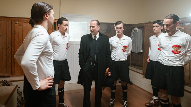 © ORF/Rizar.Photo/Gabriel Alarcon In einer historischen Umkleidekabine stehen mehrere Fußballspieler in alten Trikots um Trainer Hugo Meisl im Anzug, der eine Ansprache hält.