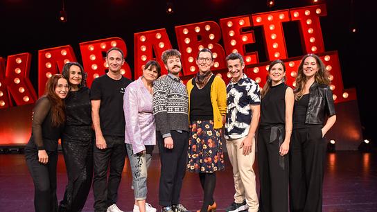© ORF/E&A Film/Hubert Mican Gernot Kulis, Eva Maria Marold, Benedikt Mitmannsgruber, Martina Schwarzmann, Omar Sarsam und "Die Kabarettgipfelband" auf der Bühne mit großem beleuchteten "Kabarettgipfel"-Schriftzug.