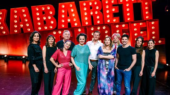 Andreas Vitasek, Kernölamazonen,  Gery Seidl, Malarina, Matthias Dieser, Alain Frei und die  Kabarettgipfelband posieren auf der Bühne vor dem leuchtenden Schriftzug „Kabarettgipfel“.
