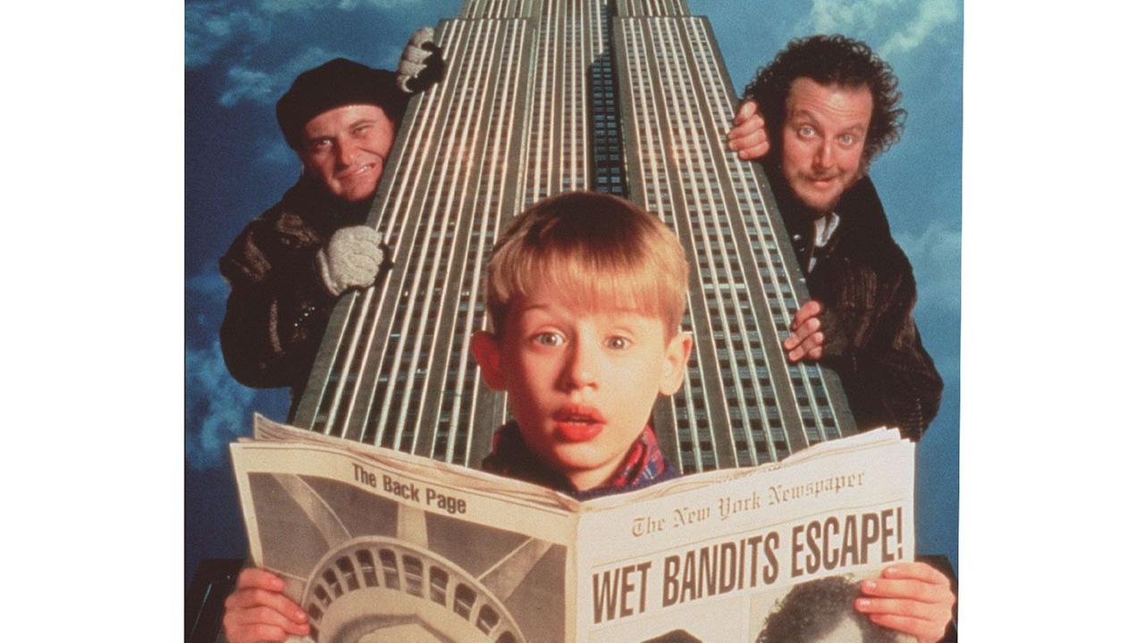 © ORF/BT Macauly Culkin hat als Kevin eine Zeitung mit der Schlagzeile 'Wet Bandits Escape!' in den Händen, hinter ihm halten sich zwei Männer in Winterkleidung an einem Wolkenkratzer fest