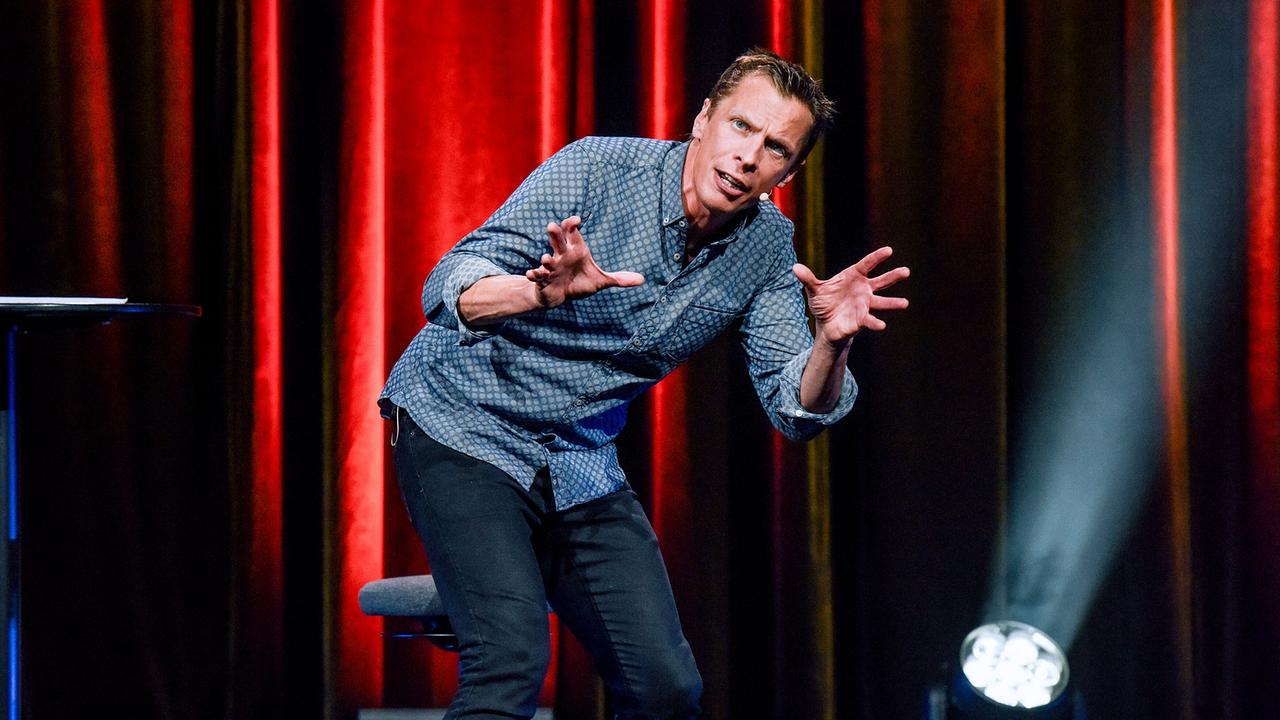 Klaus Eckel mit seinem Programm "Wer langsam spricht, dem glaubt man nicht" auf der Bühne vor einem roten Samtvorhang