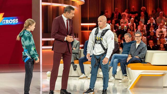 Vor dem "Kranhangel-Duell": Tim, Kai Pflaume und Fabian Hambüchen mit Sicherheitsgurt stehen vor einem Publikum.