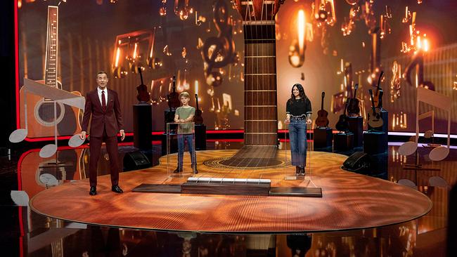 Kai Pflaume mit Benedict und Amy Macdonald stehen auf einer Bühne mit übergroßem Gitarrenhals und musikalischer Dekoration.