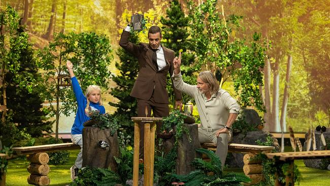 Sophia (9), Kai Pflaume und Richard David Precht sitzen beim Vogelfeder-Duell in einer märchenhaft gestalteten Waldkulisse voller Moos, Zweigen und künstlicher Waldbewohner.