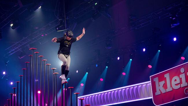 © ORF/NDR/Thorsten Jander Thomas Morgenstern beim Säulen-Sprint-Duell balanciert im Studio an hohen Stangen, gesichert durch ein Seil, vor Publikum.