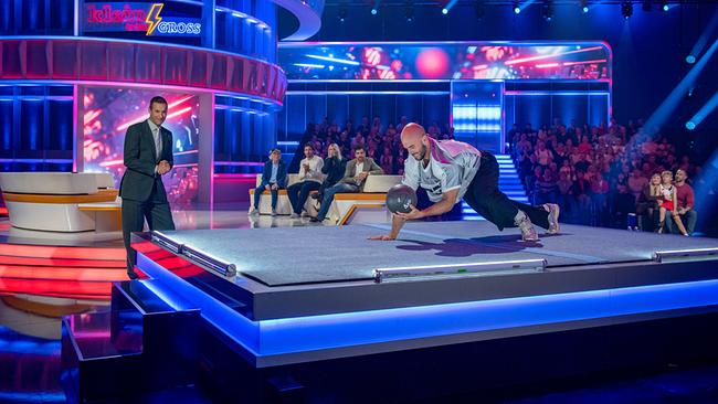 © ORF/NDR/MBTV - Produktions GmbH/Thorsten Jander Leichtathlet und Speerwerfer Julian Weber krabbelt mit einem Ball in der Hand beim Vierfüßler-Ball-Duell. Moderator Kai Pflaume steht daneben.